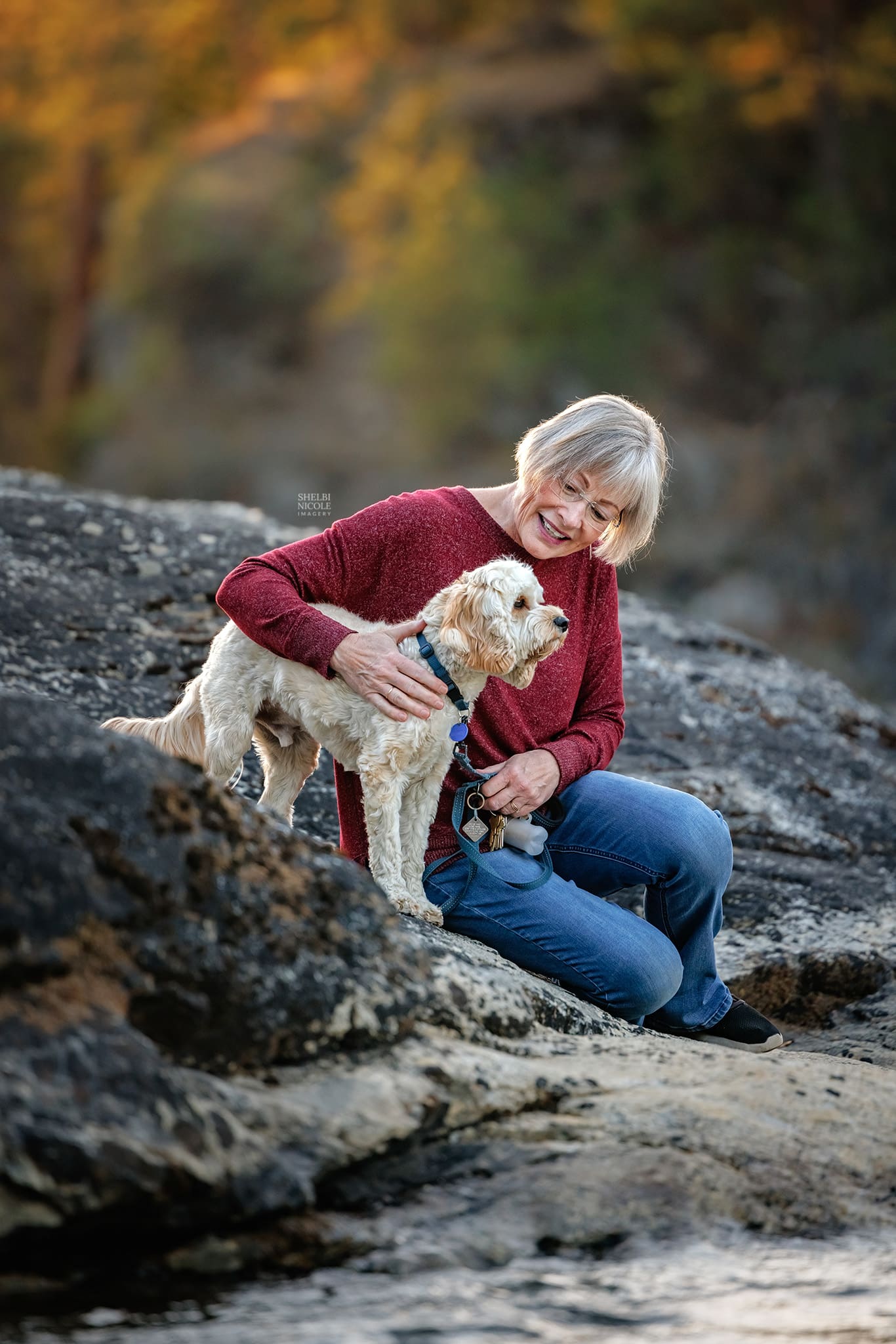 Teri sitting on a rock along the Spokane River at sunset with her small dog Teddy